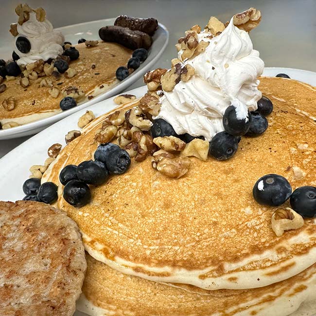 Pancakes with whipped cream, blueberries, walnuts, sausage, and a drink at our Sports Bar & Grill.