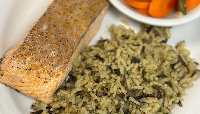 Restaurant-style seasoned salmon fillet with wild rice, carrots, and green beans on a plate.