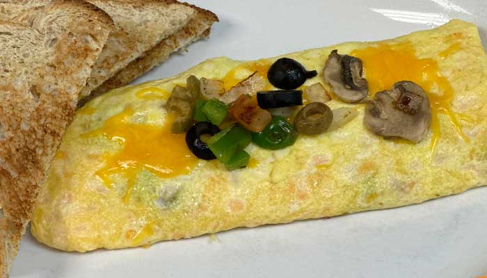 Restaurant-style omelette with cheese, mushrooms, olives, and peppers, served on toasted bread.