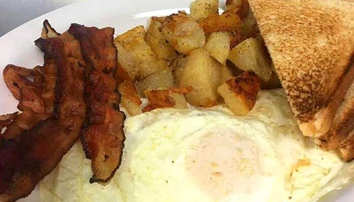 Bacon, fried eggs, home fries, and toast served on a white plate at Features Sports Bar & Grill.