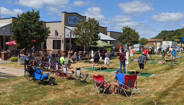 People enjoy food and drinks outdoors near Features Sports Bar & Grill under a sunny sky.