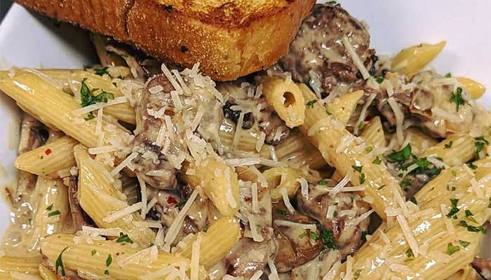 Creamy penne pasta with mushrooms, herbs, and cheese—perfect restaurant food with toasted bread.