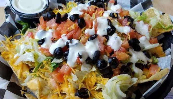 A plate of nachos at our bar, topped with cheese, veggies, and perfect for a sports drink.